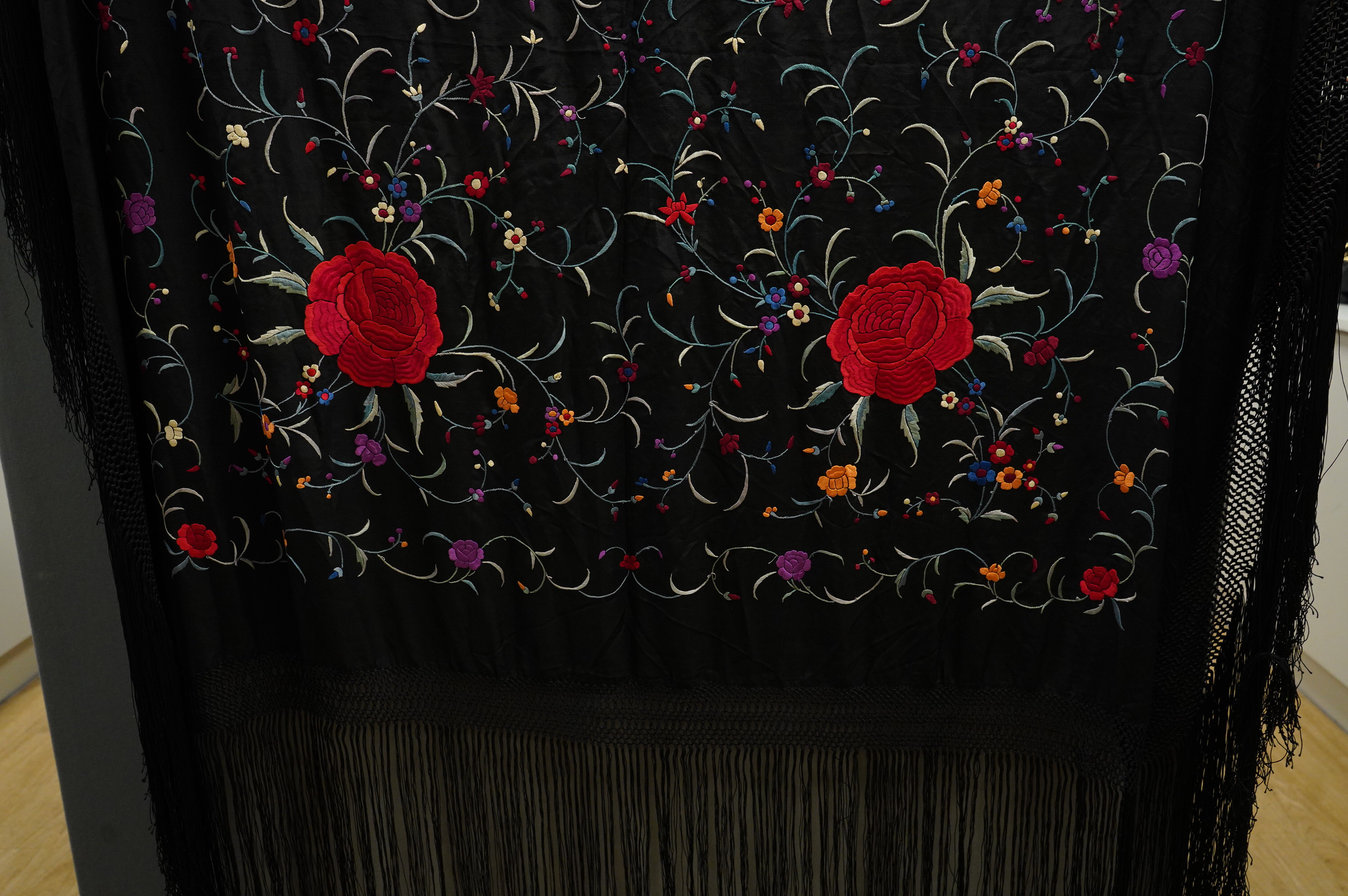 A late 19th century Chinese black silk polychrome floral embroidered shawl with long silk fringing. Embroidered with large red roses and an all over multi coloured floral sprig design. 123cm x 108cm. Condition, silk and